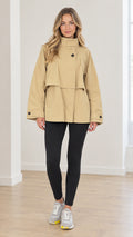 Front full view of woman wearing khaki high neck layered short trench coat with black leggings