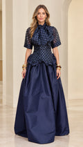 Model wearing navy blue polka dot bow neck peplum evening gown - front view