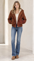 Front view of woman wearing a brown fleece-lined hooded bomber jacket with blue flared jeans