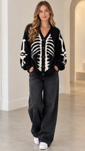 Front view of model wearing black skeleton graphic knit button-front cardigan with wide-leg jeans
