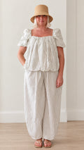 Front view of woman wearing white striped square neck puff sleeve top and lantern pants set