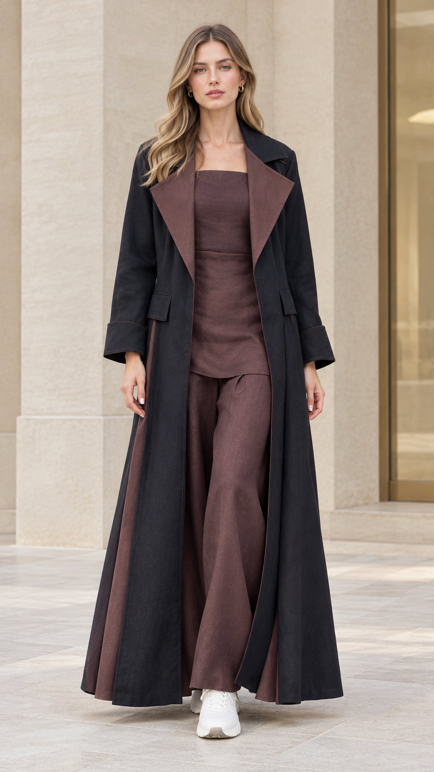 Front full-length view of model wearing black maxi flared trench coat with brown contrast lapel