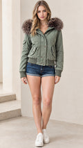 Front full-length view of model wearing olive green hooded bomber jacket with faux fur trim