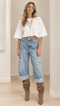 Model wearing white boxy cropped t-shirt and light-wash distressed cuffed denim jeans with slouchy boots - front view