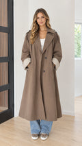 Front full-length view of model wearing taupe brown oversized maxi trench coat with turned ribbed cuffs