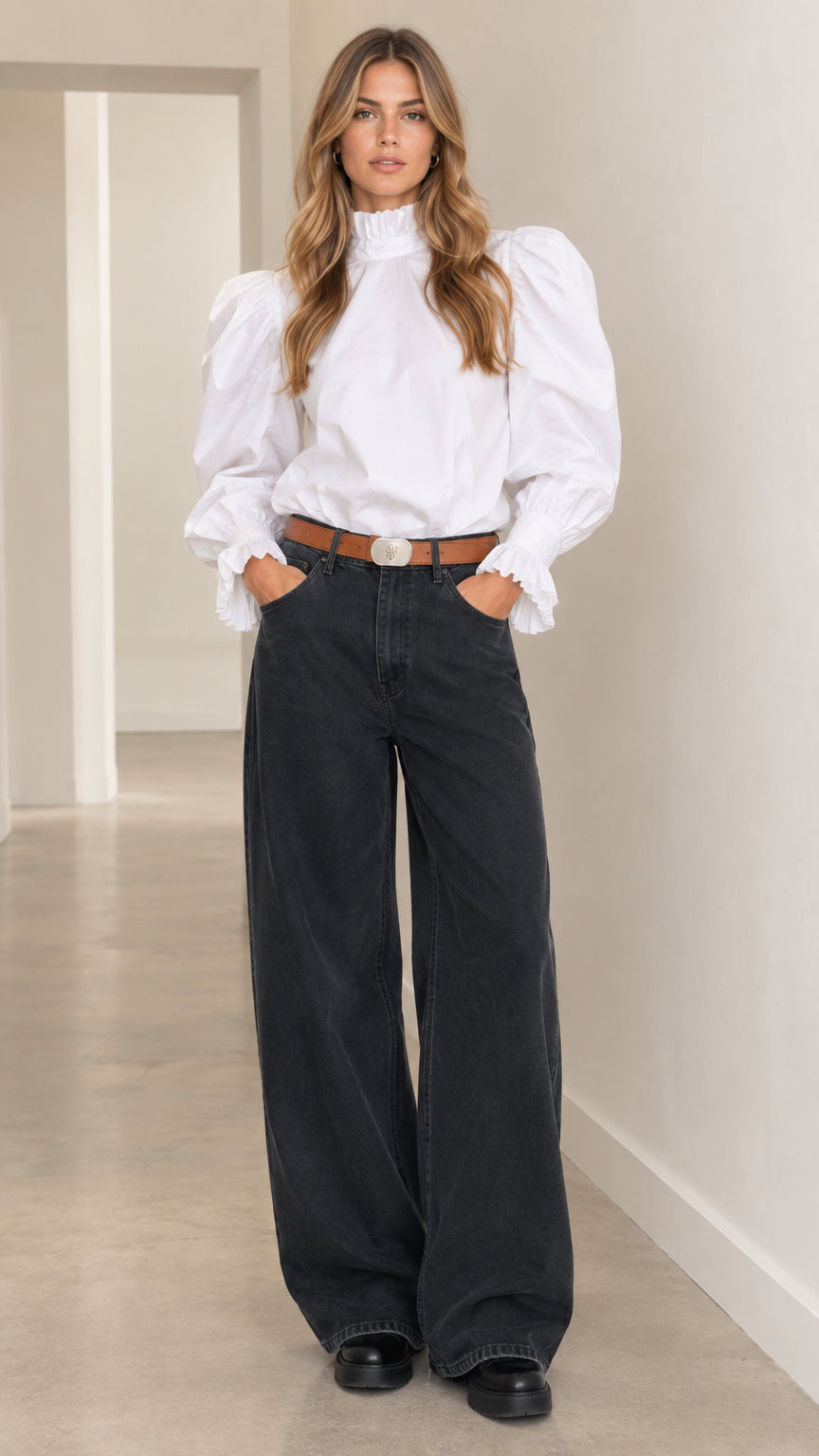 Front view of woman wearing white ruffle high-neck puff-sleeve blouse and dark wide-leg pants with brown belt