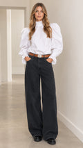 Front view of woman wearing white ruffle high-neck puff-sleeve blouse and dark wide-leg pants with brown belt