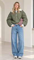 Front full-length view of model wearing olive green cropped puffer bomber jacket with white fleece collar and wide leg jeans
