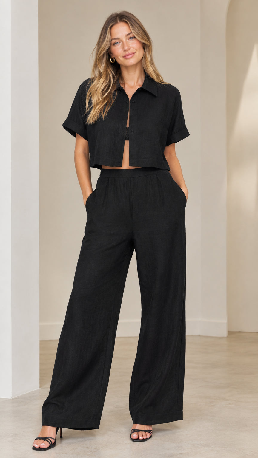 Front full view of woman wearing black cropped short-sleeve shirt and matching wide-leg trousers set