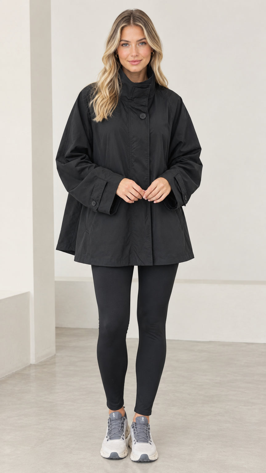 Front view of model wearing black stand collar A-line swing trench jacket with leggings