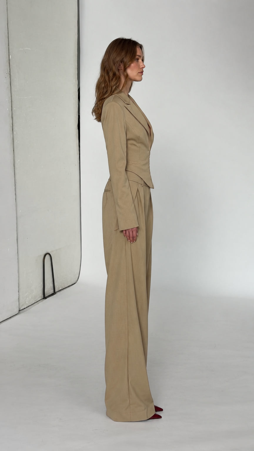 Side profile view of model wearing beige tailored cropped jacket and pleated wide-leg pants