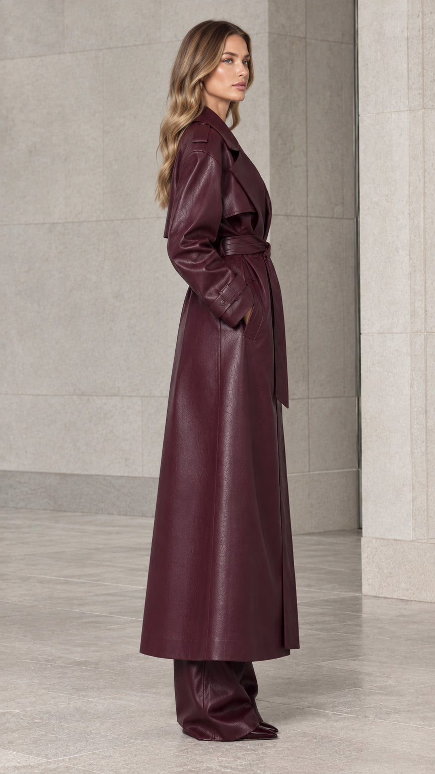 Side profile of model wearing the floor-length burgundy faux leather trench coat
