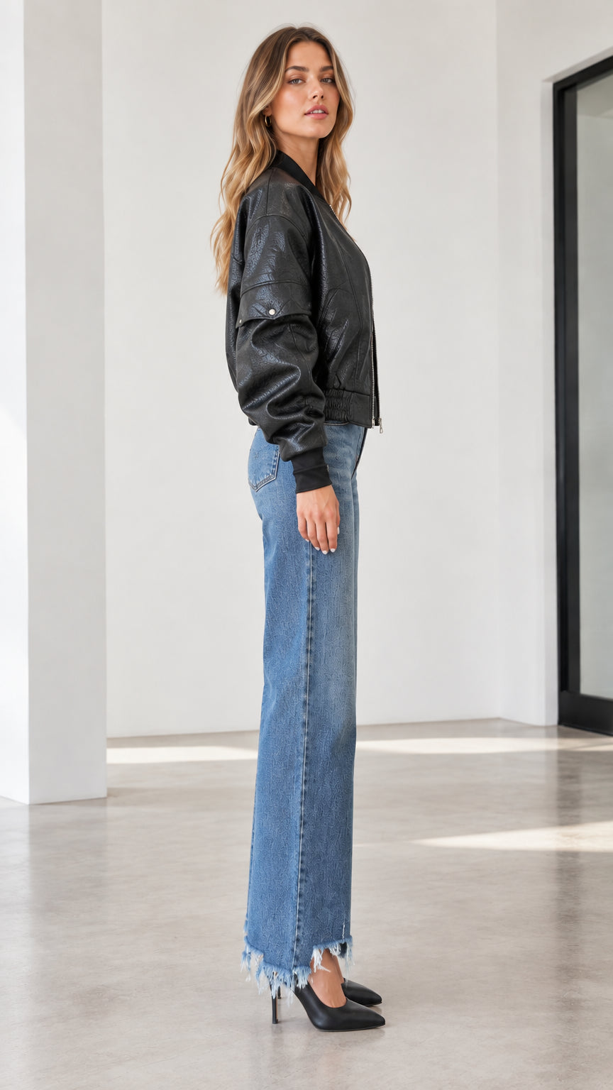 Side profile of a model wearing a black faux leather bomber jacket and wide-leg jeans