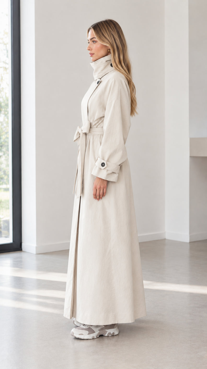 Side profile view of woman wearing beige full-length maxi trench coat