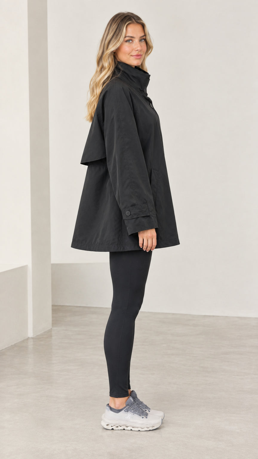 Side profile view of model wearing black swing trench coat showing trapeze silhouette