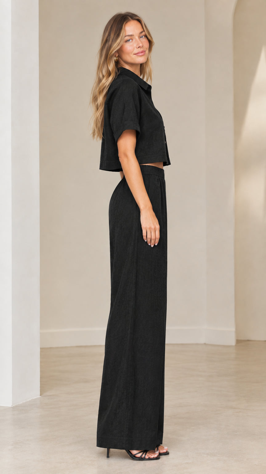 Side profile view of woman modeling black two-piece cropped shirt and high-waist pants set