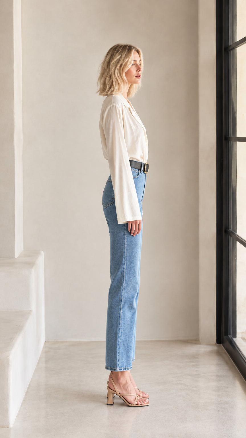 Side profile view of woman wearing cream flare sleeve blouse and light wash jeans