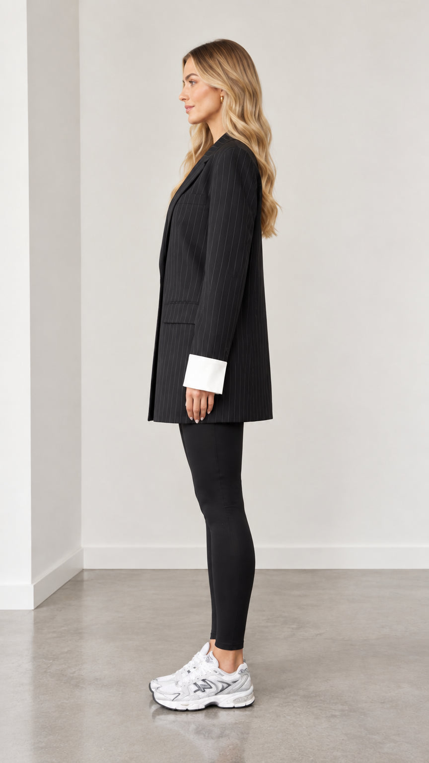 Side profile view of woman wearing black oversized pinstripe blazer with white foldover cuffs