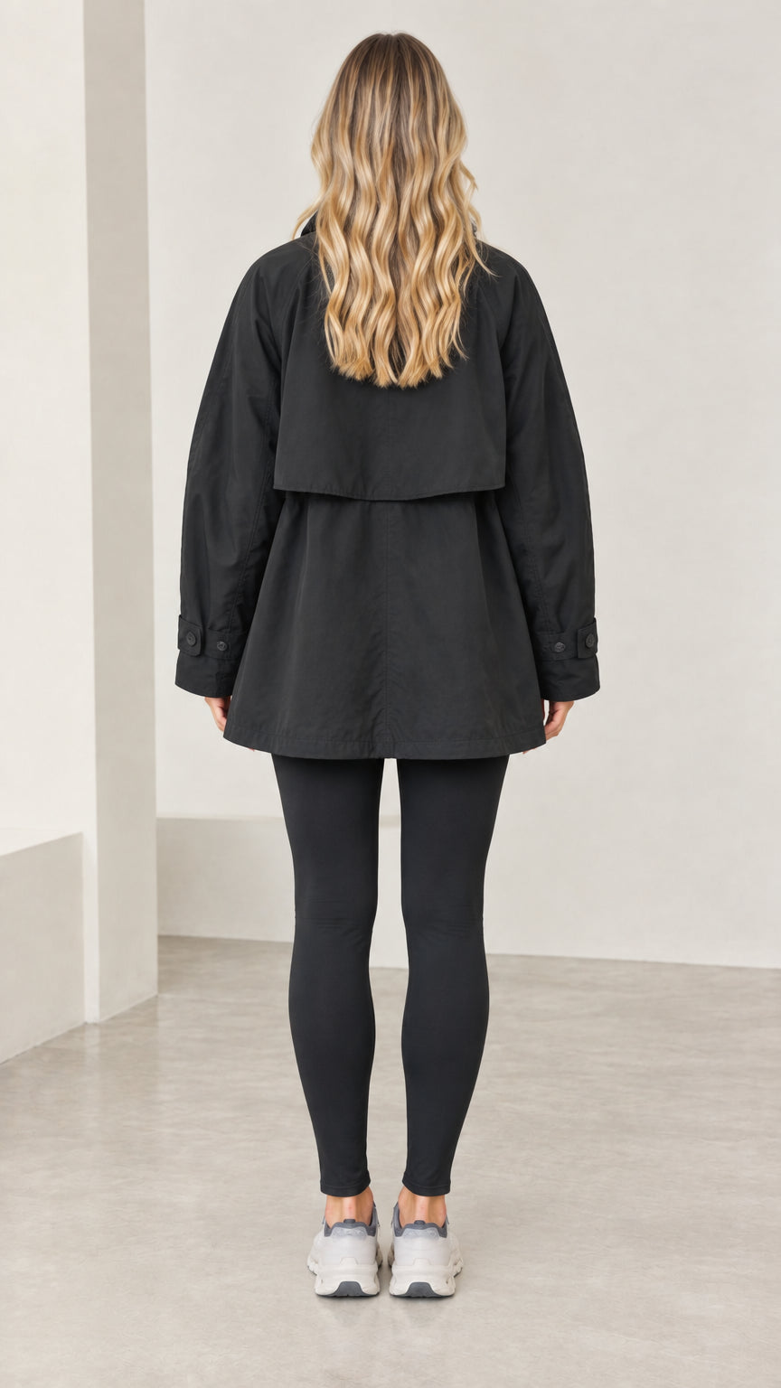 Back view of model wearing black A-line jacket showing back storm flap overlay