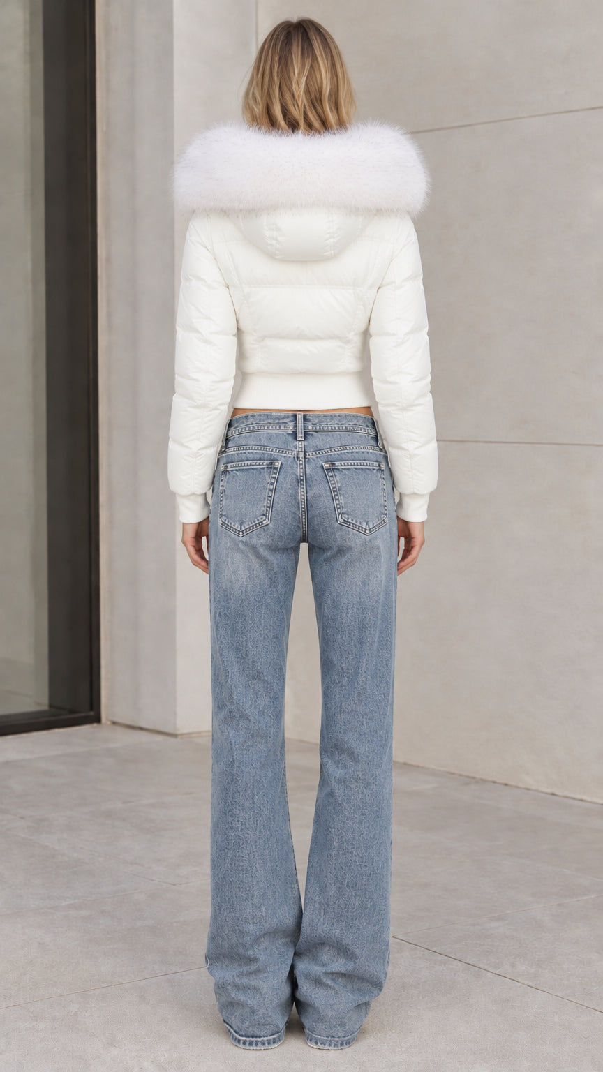 Back view of model wearing white cropped hooded puffer jacket with wide leg denim