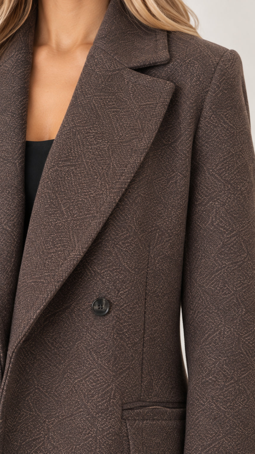 Close-up detail of the brown maxi coat showing textured weave fabric and notch lapel