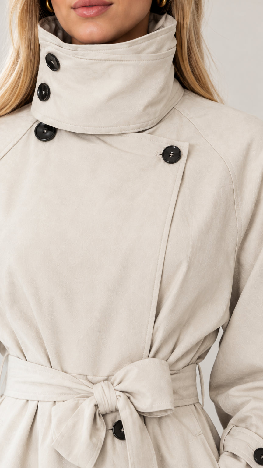 Close-up detail of high collar, buttons, and tied belt on beige trench coat